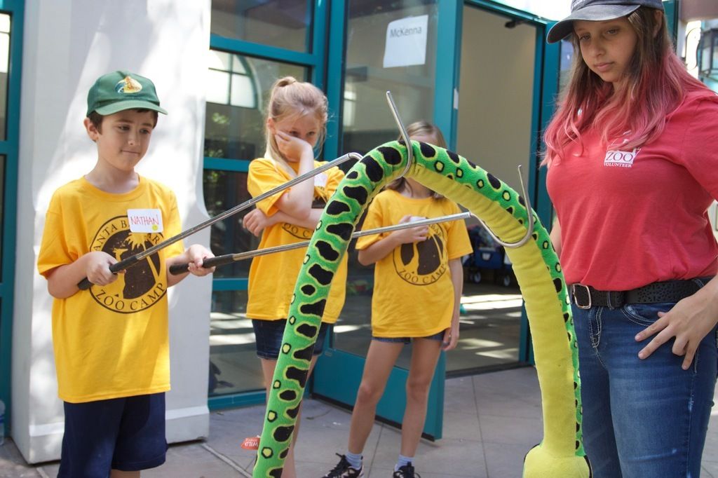 a young boy handles a plush snake while two young girls look on